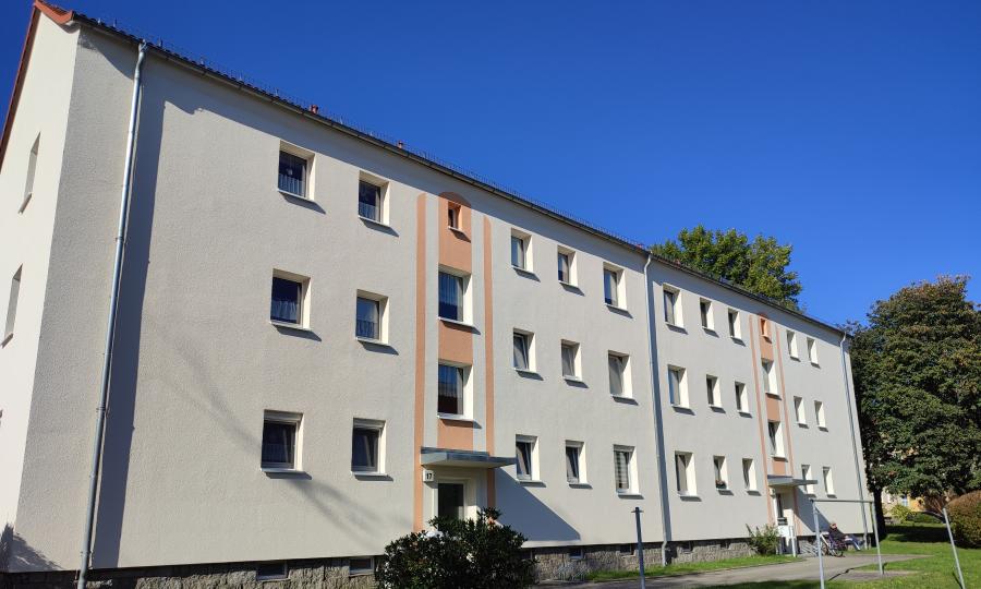 Mehrfamilienhaus mit heller Fassade, regelmäßig angeordneten Fenstern und kleinem Vorgarten mit Rasenfläche