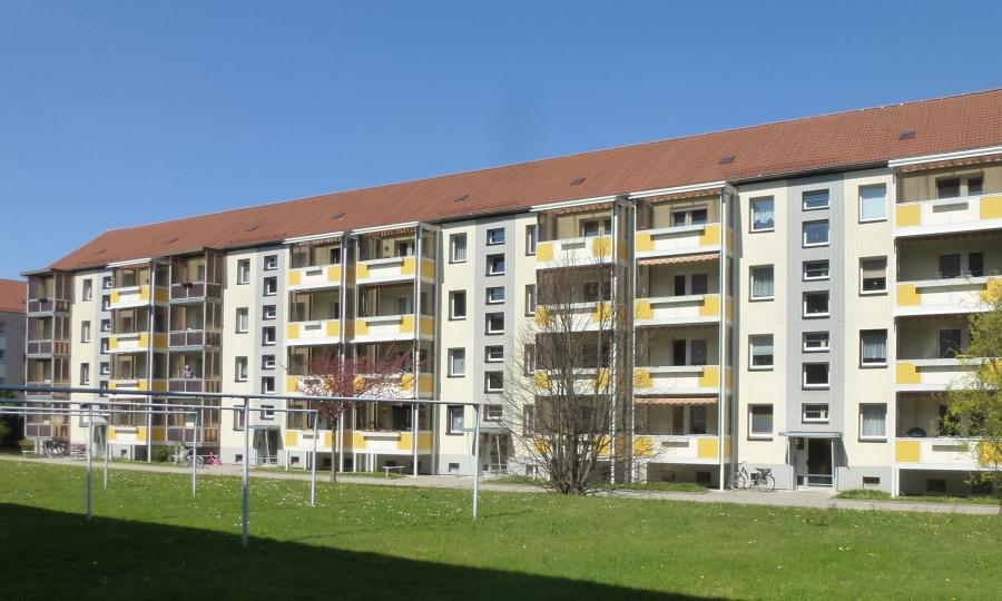 Mehrgeschossiges Wohnhaus mit hellen Fassaden und gelben Balkonakzenten, davor eine große Grünfläche