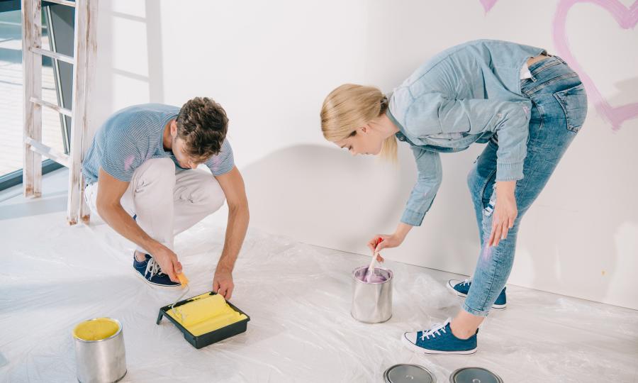 Junges Paar mit Pinsel und Roller bückend über Farbbehältern