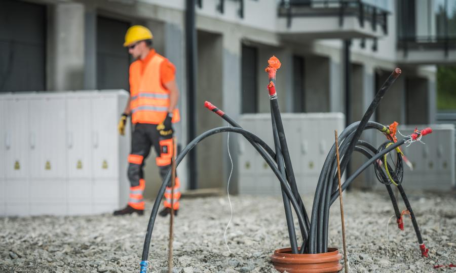 Glasfaserkabel aus der Erde rankend, im Hintergrund ein Bauarbeiter